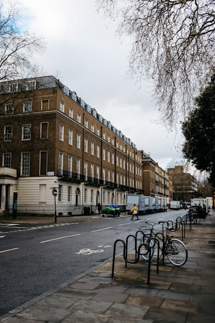 A medium-sized commercial refuse collection vehicle is parked on the street in front of a historic, multi-storey brick building with large, arched windows and detailed stonework in the heart of Knight