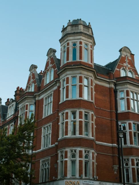 A tall, historic red-brick building with multiple white-framed sash windows arranged in vertical rows, and decorative architectural details including stone trim and a small turret at the top. The buil